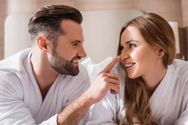 Hombre sonriente en albornoz tocando la nariz de la novia en el hotel - foto de stock