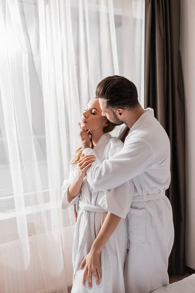 Mann im Bademantel berührt Freundin in Hotelfenster — Stockfoto