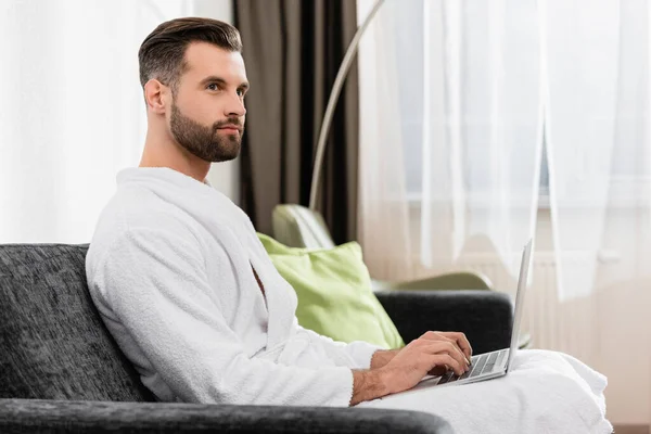 Freelancer em roupão branco usando laptop no quarto de hotel — Fotografia de Stock