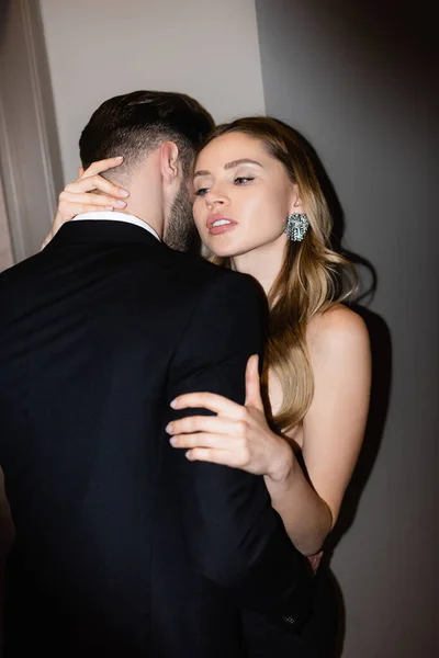 Mulher sedutora abraçando namorado de terno no quarto de hotel durante a noite — Fotografia de Stock
