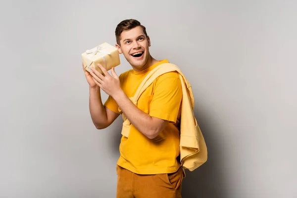 Homem animado segurando caixa de presente no fundo cinza — Fotografia de Stock