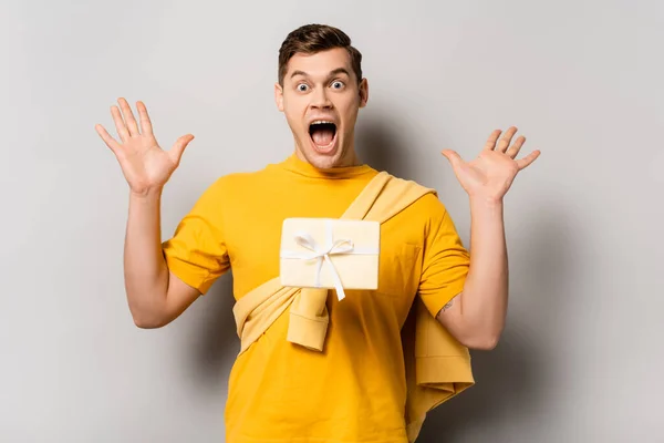 Homme étonné debout près de la boîte-cadeau dans l'air sur fond gris — Photo de stock