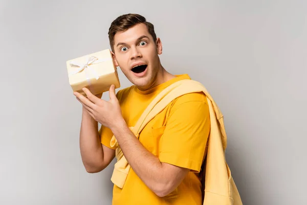 Excited man holding present near ear on grey background — Stock Photo