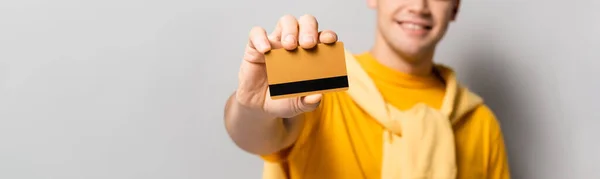 Vue recadrée de la carte de crédit en main du jeune homme floue sur fond gris, bannière — Photo de stock