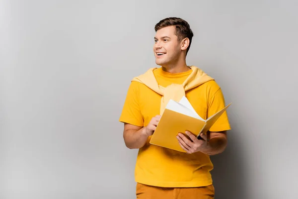 Smiling student holding notebook on grey background — Stock Photo