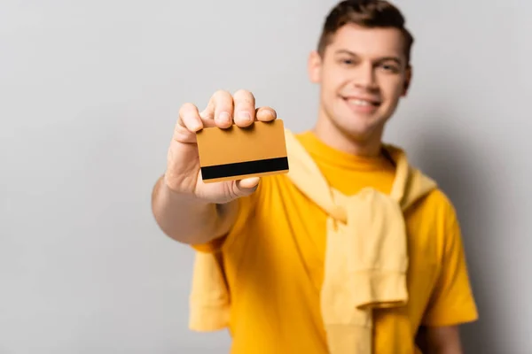 Cartão de crédito na mão do homem sorridente borrado em fundo cinza — Fotografia de Stock