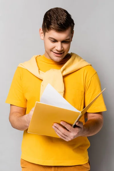 Estudiante positivo mirando cuaderno sobre fondo gris - foto de stock