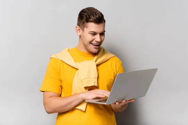 Cheerful man using laptop on grey background — Stock Photo