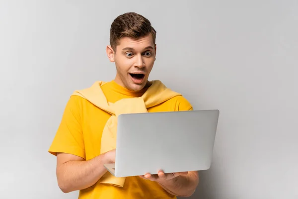 Дивовижний чоловік з відкритим ротом використовує ноутбук на сірому фоні — стокове фото