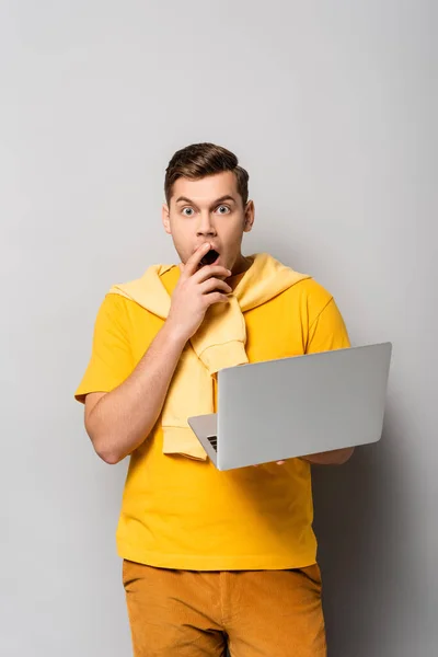 Aufgeregter Mann blickt in Kamera, während er Laptop auf grauem Hintergrund hält — Stockfoto