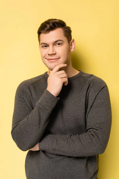 Jovem de pulôver cinza sorrindo para a câmera no fundo amarelo — Fotografia de Stock