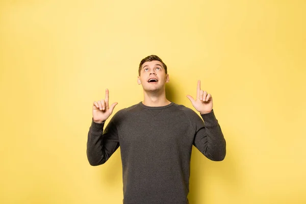 Hombre señalando con los dedos hacia arriba sobre fondo amarillo - foto de stock