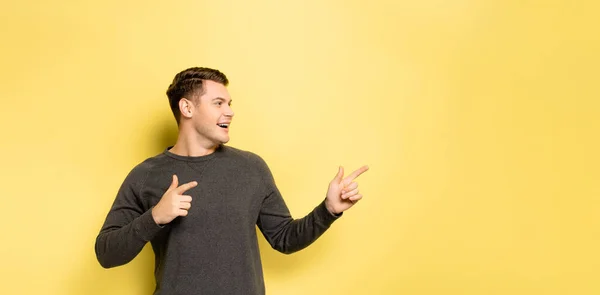 Young man pointing with fingers on yellow background, banner — Stock Photo