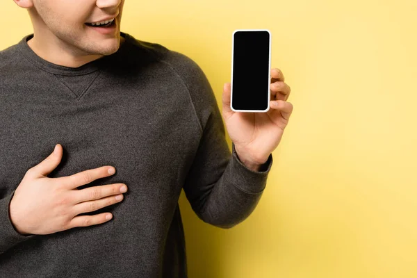 Vista recortada del hombre positivo sosteniendo el teléfono inteligente con pantalla en blanco sobre fondo amarillo - foto de stock