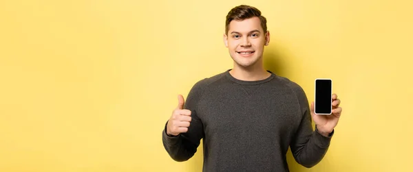 Man smiling at camera while holding cellphone with blank screen on yellow background, banner — Stock Photo