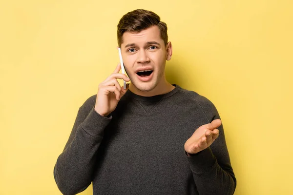 Verwirrter Mann zeigt mit der Hand auf Kamera, während er auf gelbem Hintergrund auf Smartphone spricht — Stockfoto