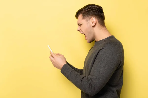 Vista lateral del hombre gritando usando el teléfono celular sobre fondo amarillo - foto de stock