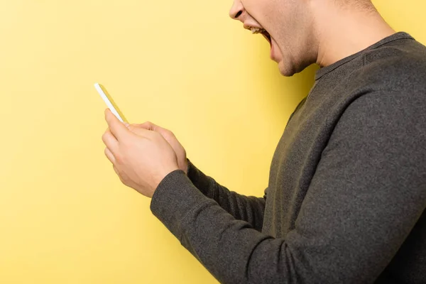 Vista recortada del hombre agresivo utilizando el teléfono inteligente sobre fondo amarillo - foto de stock