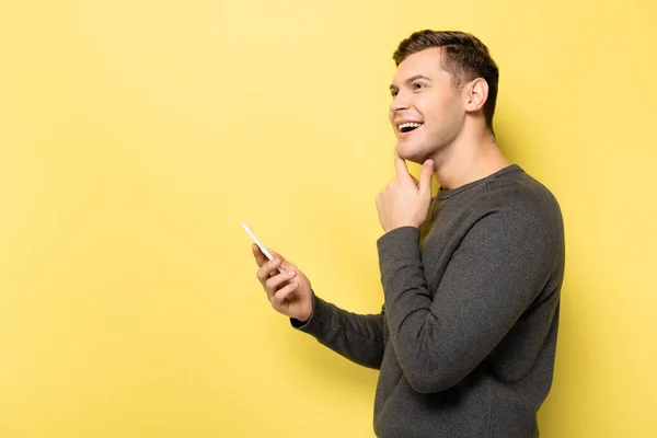 Hombre sonriente usando teléfono inteligente sobre fondo amarillo con espacio de copia - foto de stock