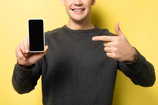 Vista cortada do homem segurando smartphone com tela em branco e apontando com o dedo no fundo amarelo — Fotografia de Stock