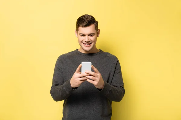 Homme souriant tenant un téléphone portable sur fond jaune — Photo de stock