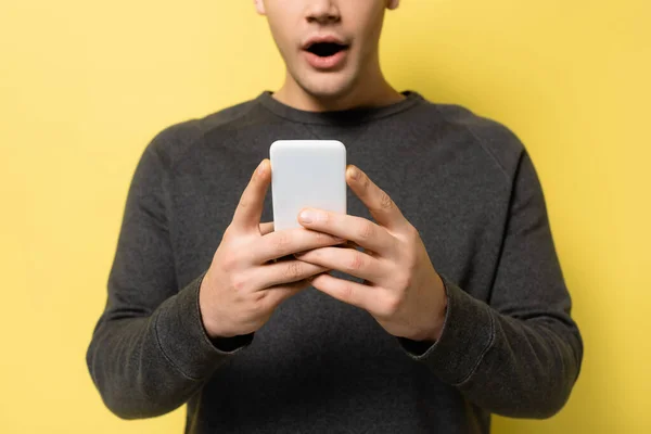 Vista cortada do smartphone em mãos de homem animado borrado no fundo amarelo — Fotografia de Stock