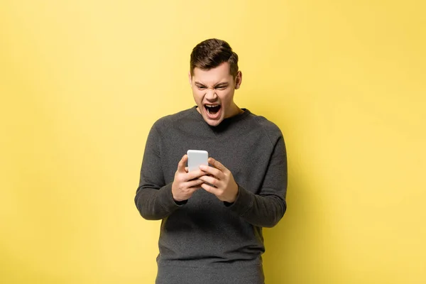 Irritado homem gritando ao usar celular no fundo amarelo — Fotografia de Stock