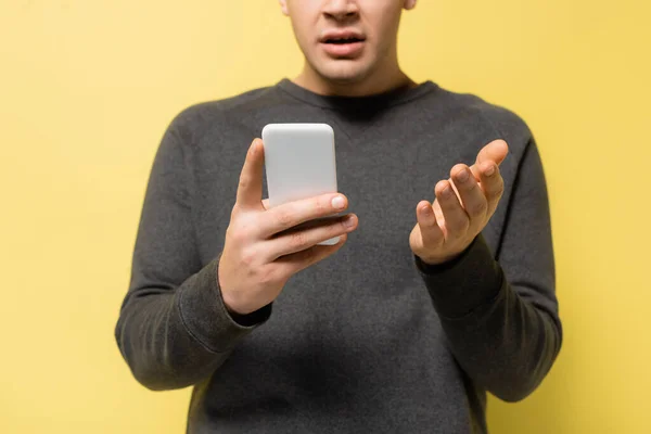 Cropped view of man pointing with hand while using smartphone on yellow background — Stock Photo