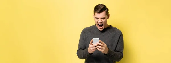 Screaming and angry man using cellphone on yellow background, banner — Stock Photo