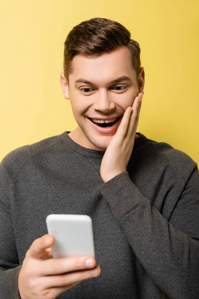 Glücklicher Mann mit Hand vor der Wange, Smartphone auf verschwommenem Vordergrund auf gelbem Hintergrund — Stockfoto