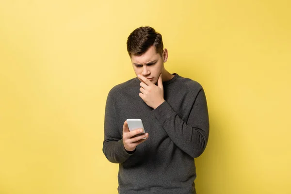 Homem pensativo olhando para o smartphone no fundo amarelo — Fotografia de Stock
