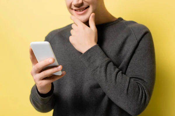 Vista recortada del teléfono inteligente en la mano del hombre sonriente borrosa sobre fondo amarillo - foto de stock