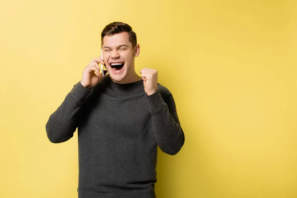 Aufgeregter Mann zeigt Ja-Geste beim Gespräch auf Smartphone auf gelbem Hintergrund — Stockfoto