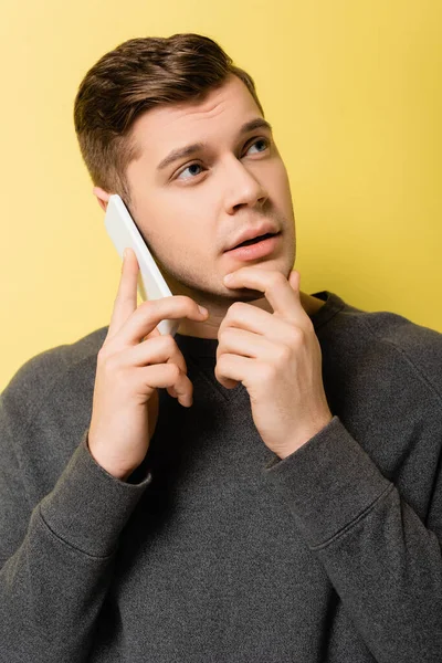 Homem sonhador falando no telefone celular no fundo amarelo — Fotografia de Stock