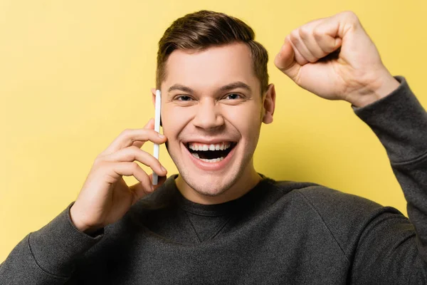 Homem alegre mostrando sim gesto e falando no celular no fundo amarelo — Fotografia de Stock