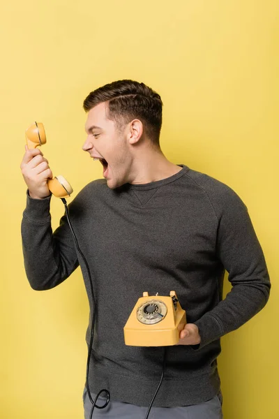 Человек кричит на телефон на желтом фоне — стоковое фото