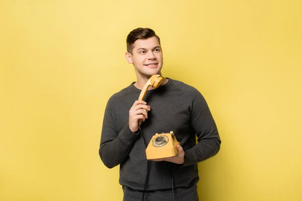 Homme souriant tenant un téléphone rétro sur fond jaune — Photo de stock