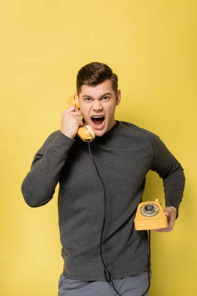 Раздражённый мужчина разговаривает по телефону на жёлтом фоне — стоковое фото