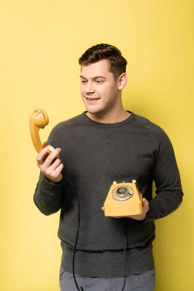 Junger Mann lächelt, während er auf Telefonhörer auf gelbem Hintergrund blickt — Stockfoto