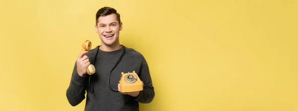 Hombre positivo sosteniendo teléfono sobre fondo amarillo con espacio de copia, banner - foto de stock