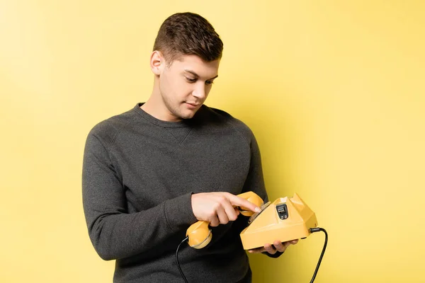 Young man in grey pullover using vintage telephone on yellow background — Stock Photo