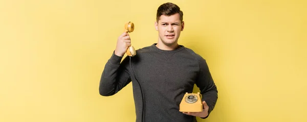 Confused man holding retro telephone on yellow background, banner — Stock Photo