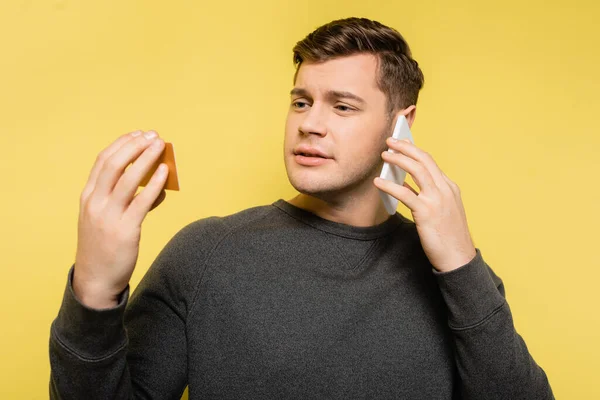 Man talking on telephone and looking at credit card on yellow background — Stock Photo