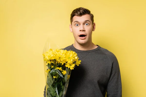 Uomo stupito con bouquet guardando la fotocamera su sfondo giallo — Foto stock