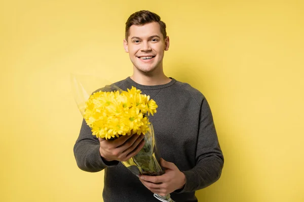 Hombre alegre sosteniendo flores sobre fondo amarillo - foto de stock