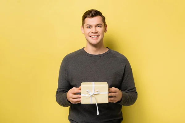 Sorrindo homem com caixa de presente olhando para a câmera no fundo amarelo — Fotografia de Stock