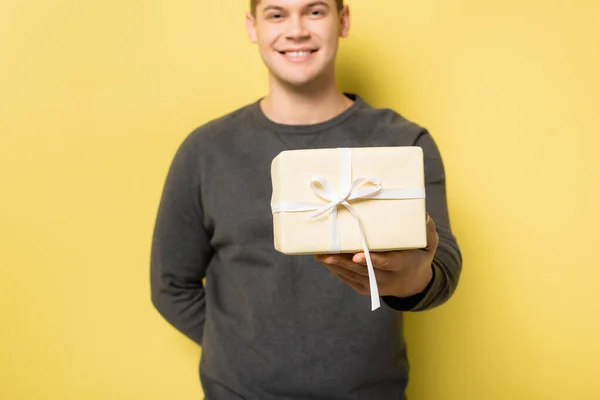 Caixa de presente na mão do homem sorridente borrada no fundo amarelo — Fotografia de Stock