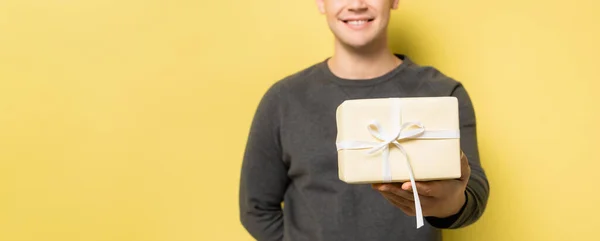 Vue recadrée du présent en main d'un homme souriant flou sur fond jaune, bannière — Photo de stock