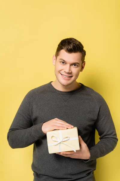Happy man with present looking at camera on yellow background — Stock Photo