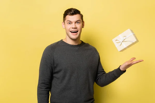 Lächelnder Mann wirft Geschenkbox auf gelbem Hintergrund — Stockfoto